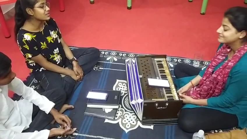 A vocal lesson at the academy, harmonium on the floor between teacher and students