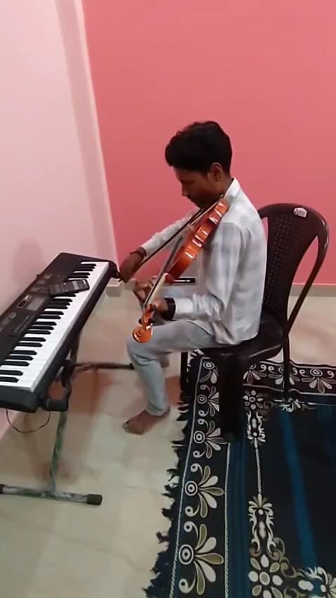 A student practising violin beside a keyboard at the academy